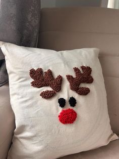 a white pillow with red nose and antlers embroidered on it sitting on a couch