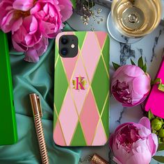 a pink and green phone case sitting on top of a table next to some flowers