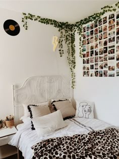 a white bed topped with lots of pillows next to a wall covered in pictures and plants