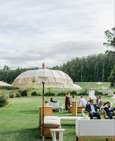 people are sitting on lawn chairs under an umbrella in the middle of a grassy area