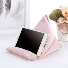 a cell phone sitting on top of a pink pillow next to a vase with flowers