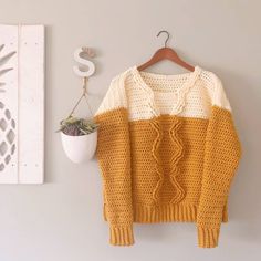 a yellow and white sweater hanging on a wall next to a potted succulent