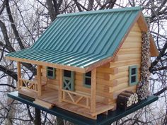 a small log cabin with a green roof and porch is perched on top of a tree