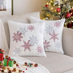 two christmas pillows sitting on top of a couch next to a christmas tree and presents