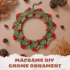 a knitted wreath with red flowers and pine cones around it on top of a piece of paper