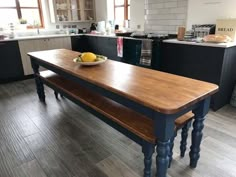 a wooden table sitting in the middle of a kitchen next to a bowl of fruit