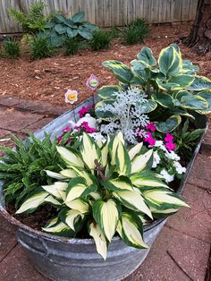 a metal tub filled with lots of flowers on top of a brick floor next to a wooden fence