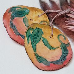 two ceramic ornaments are sitting next to each other on a white surface with pink and green feathers