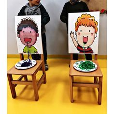 two children standing next to each other in front of paintings on wooden chairs with faces painted on them