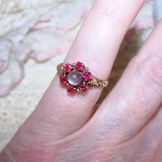 Dating To The Late 1880s/1890s Or So, May I Offer This 14k Rose Gold (Tested, Not Marked) Engagement Ring - Sweetheart Ring - Fashion Ring Featuring A Top Design Of 2mm Faceted Round Pink/Red Quartz (Tested) Acting As A Halo Around A 4.5mm Moonstone Cab. The "Florette" Design On The Top Measures 3/8" High/Wide; Ring Size Is A 5 On My Sizer. Weight Is 2 Grams. There's A Lovely Bit Of Repousse Work To Either Side Of The Center Design. The Inside Shank Of The Ring Is Unmarked For Gold Which Was Not A Requirement To Do Until The Federal Stamping Act Of 1906 However, The Inside Of The Ring Is Designer Signed - Hm Conjoined Within A Stylized Buttercup Round. Very Fine Condition With No Problems I Quartz Engagement Ring, Red Quartz, Wide Ring, Engagement Ring Sizes, Pink Quartz, Antique Victorian, Womens Jewelry Rings, Red Gold, Fashion Rings