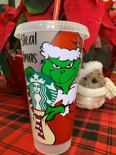 a starbucks cup with the grin on it sitting on a table next to poinsettis