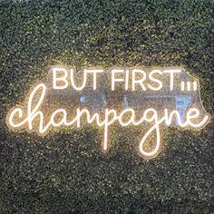 a neon sign that says but first i champagne on top of a green wall covered in ivy