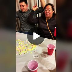 a man and woman sitting at a table with cups in front of them that are filled with candy