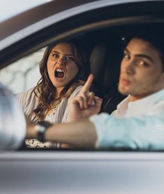 a man and woman sitting in a car pointing at something