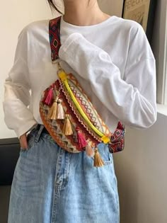 a woman wearing a white shirt and blue jeans holding a colorful handbag in front of her face