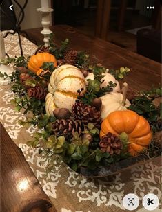 a bowl filled with pumpkins and greenery sitting on top of a wooden table