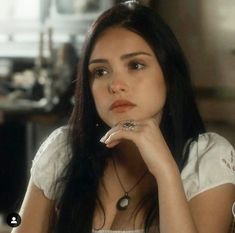 a woman sitting at a table with her hand on her chin and looking off to the side