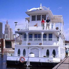 two people standing on the balcony of a houseboat in front of a cityscape