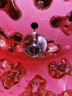 a disco ball hanging from the ceiling in front of many shiny objects on pink background