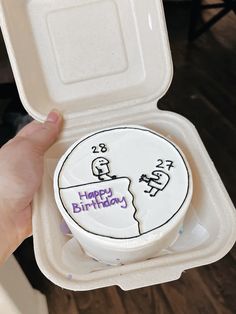 a person holding up a birthday cake in a foam container with the lid open to show it's inside