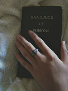 a person's hand holding a book on top of a bed with the cover pulled down