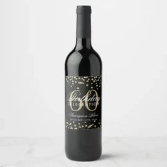 a bottle of red wine with gold confetti on the label and black cap