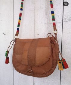 a brown purse hanging on the side of a white wooden wall with colorful tassels