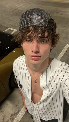 a young man wearing a baseball cap sitting in front of a black and gold car