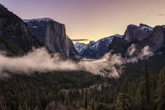 the valley is surrounded by mountains and trees with mist coming from them in the air