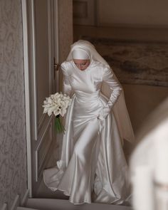 a woman in a white wedding dress is walking down the stairs holding a bouquet of flowers