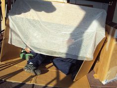 a man sitting on top of a cardboard box under a tarp covered table cloth