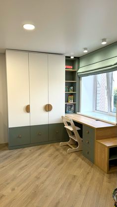 an empty room with wooden floors and white cupboards in the corner, next to a large window