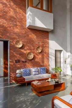 a living room filled with furniture next to a tall brick wall and windows on top of it