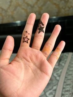 a person's hand with three small stars on the middle finger and two fingers behind them