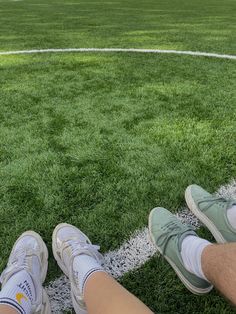 two people sitting on the edge of a soccer field with their feet up in the air