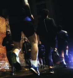 a group of people standing in front of a brick wall at night with their feet on the ground