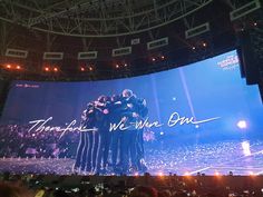 a group of people standing on top of a stage under a large screen with the words thank you we are one