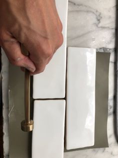 a person's hand on the handle of a white marble tile wall with gold accents