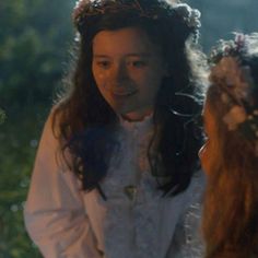 two women in white dresses standing next to each other with flowers on their head and one woman wearing a flower crown