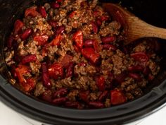 a crock pot filled with ground beef and red peppers next to a wooden spoon