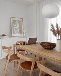 a wooden table topped with a laptop computer next to a white vase filled with flowers