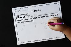 a child's hand holding a pencil over a paper with the words gravity on it