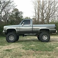 a large gray truck parked on top of a grass covered field in front of trees