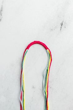 a multicolored string necklace on a marble surface with white and red beads hanging from it's end