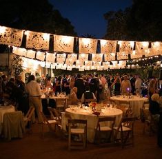 a group of people standing around tables with lights strung over them and hanging from the ceiling