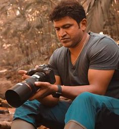 a man holding a camera in his hand while sitting on the ground next to some trees