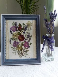 a vase filled with purple flowers next to a framed art piece on a table top