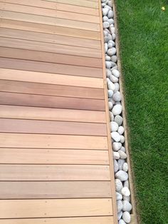 a wooden deck with white rocks and grass in the back ground, next to a lawn