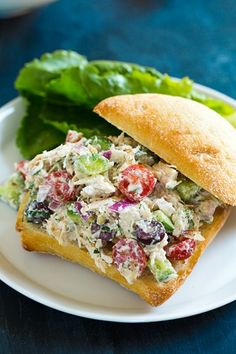 a sandwich on a white plate with lettuce and tomato salad in the middle