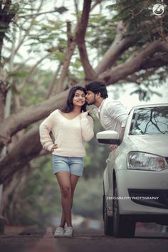 a man and woman standing next to each other in front of a car